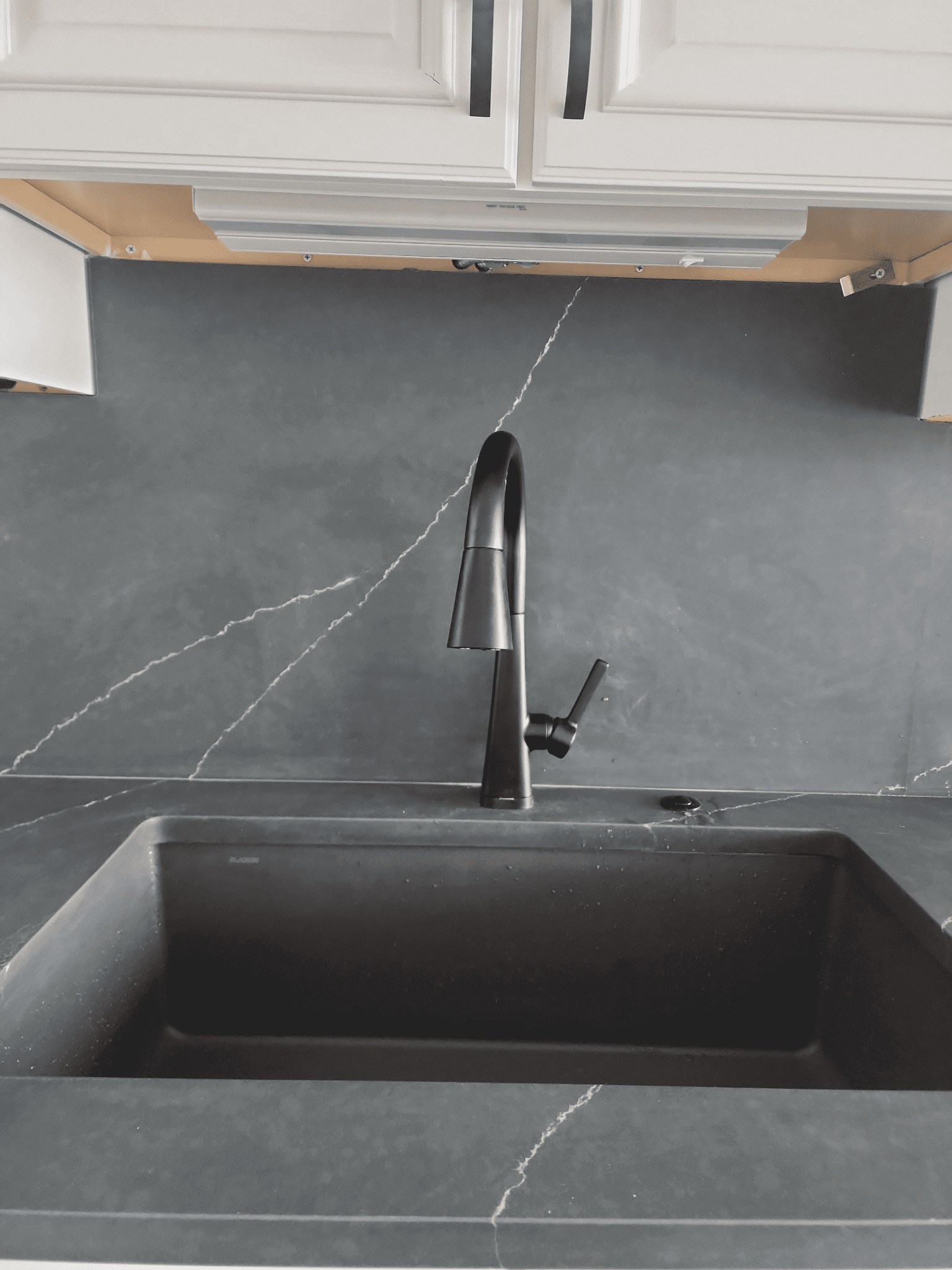 Black kitchen sink with marble backsplash.