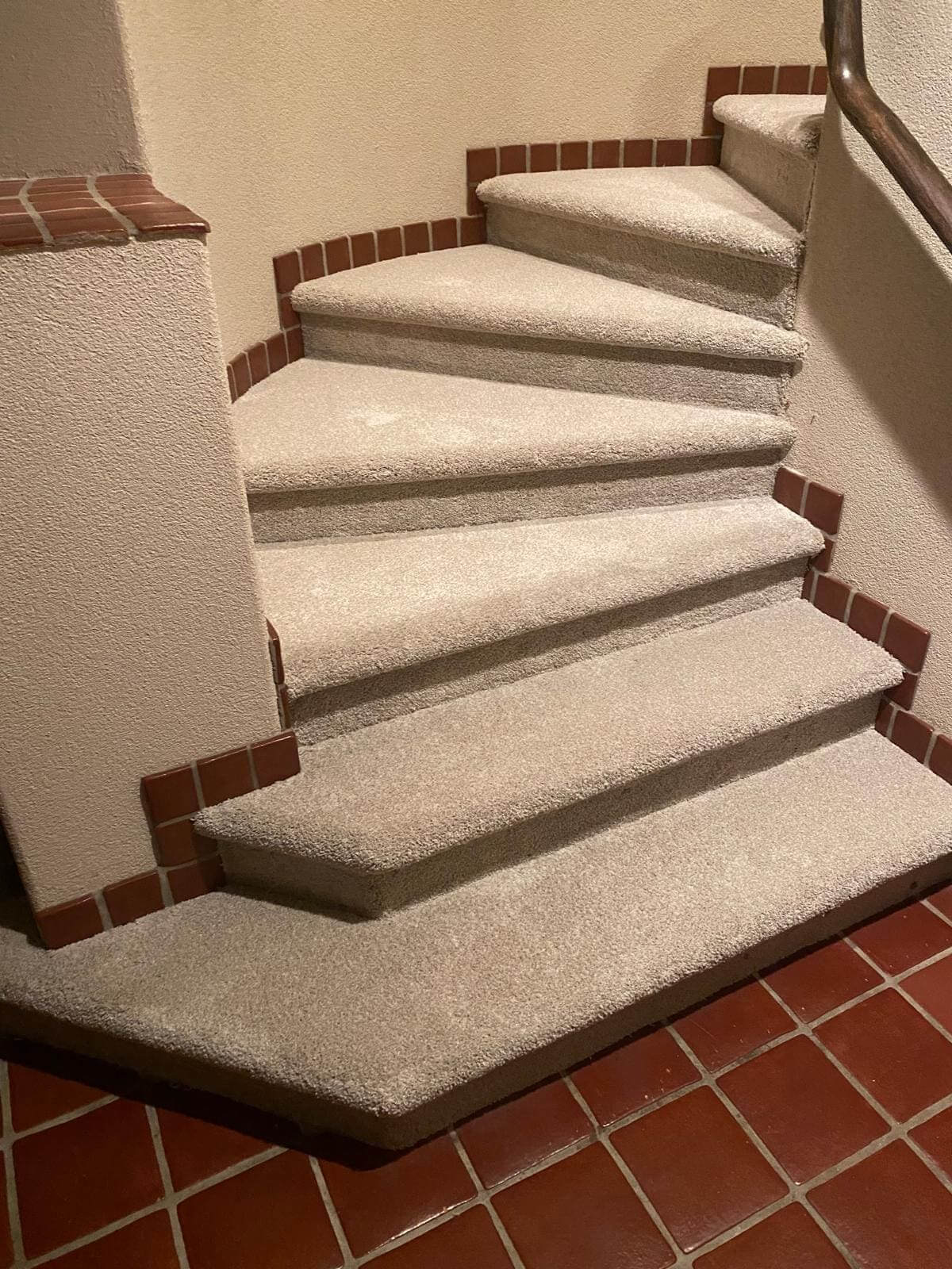 Carpeted spiral staircase with red tiles.