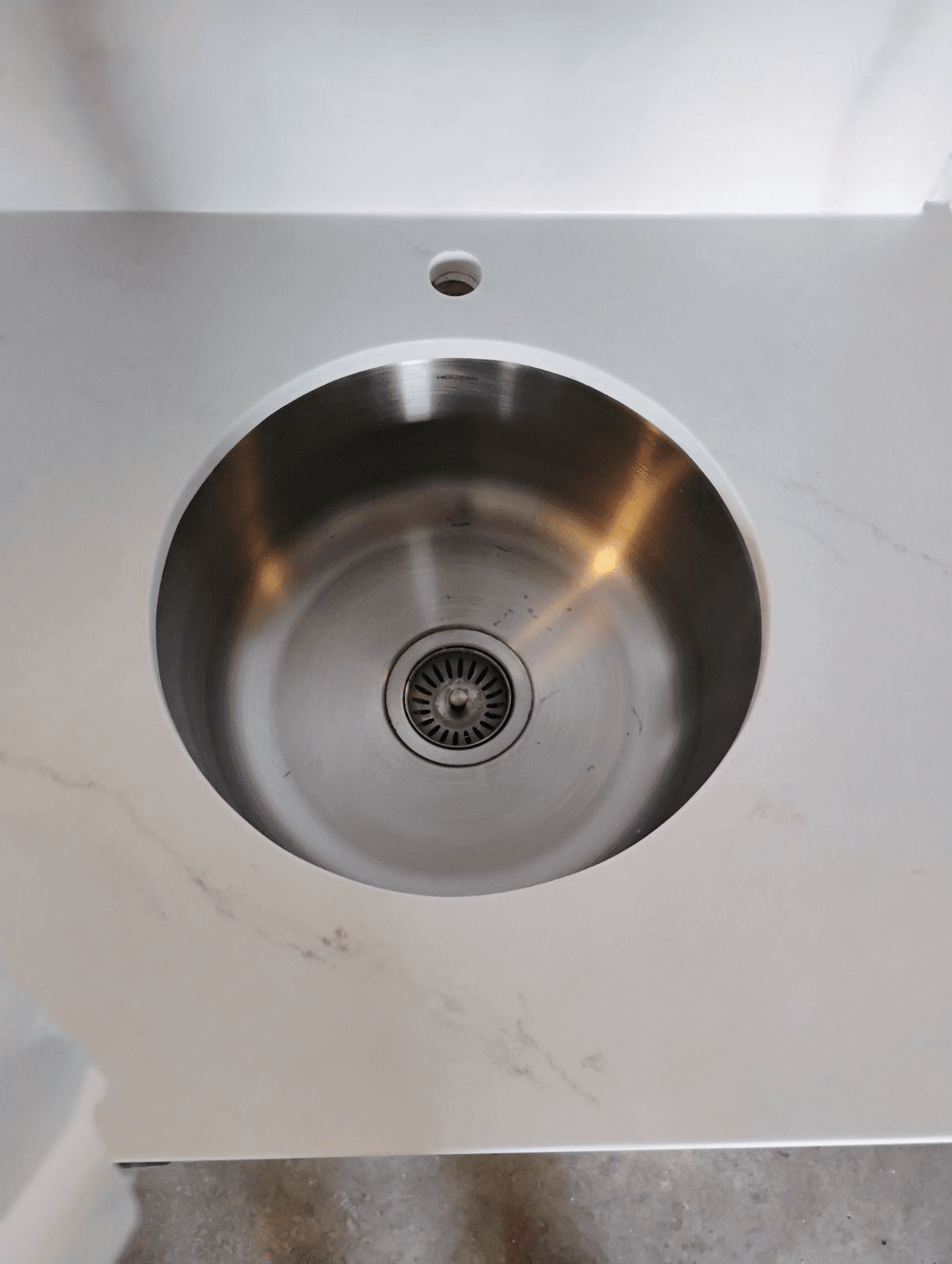 Round stainless steel sink in white countertop.