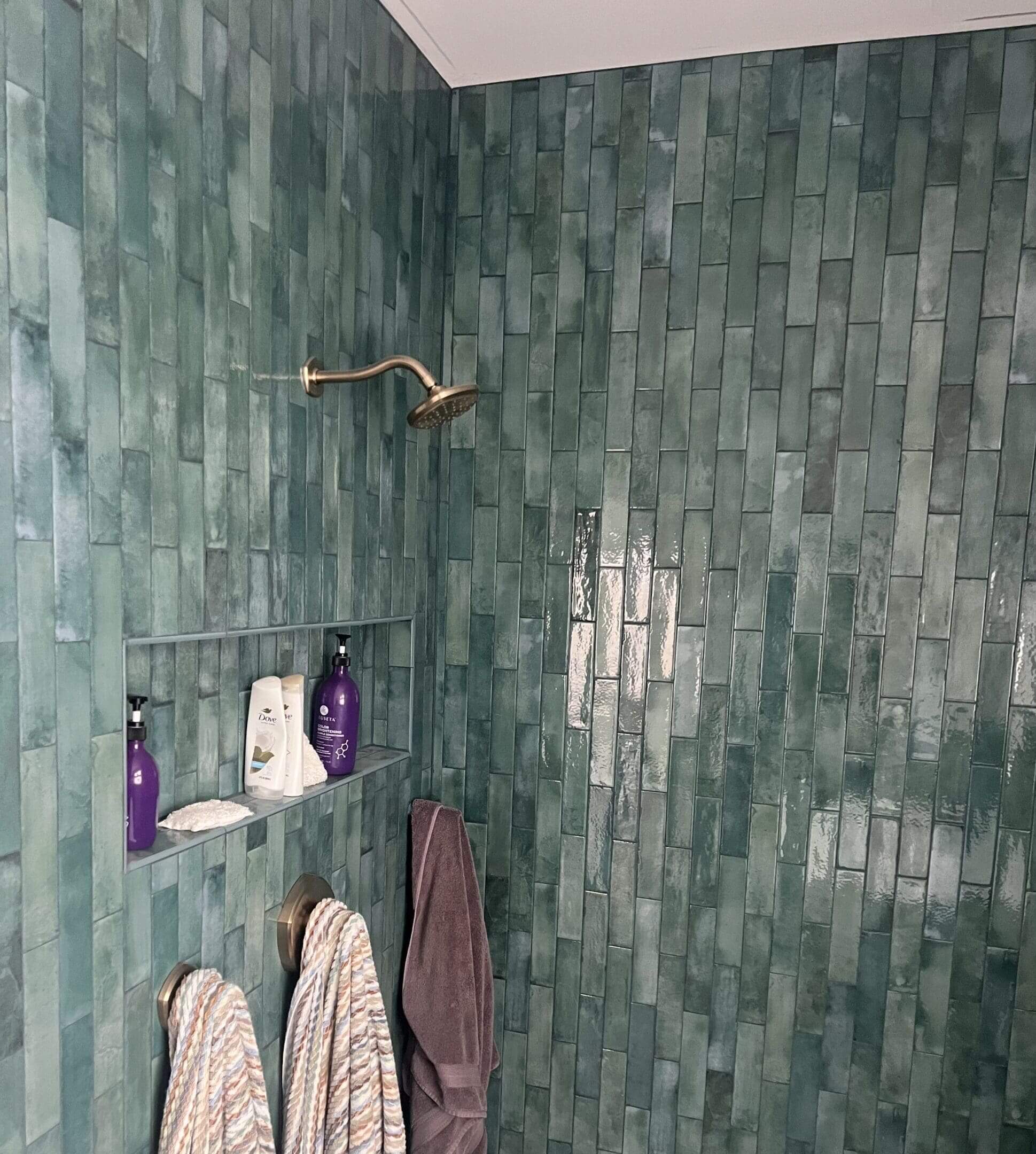 Green tiled shower with towels and products.